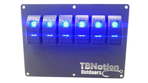 Black 6-gang TBNation Outdoors hydro-dipped aluminum switch panel with six glowing blue rocker switches.