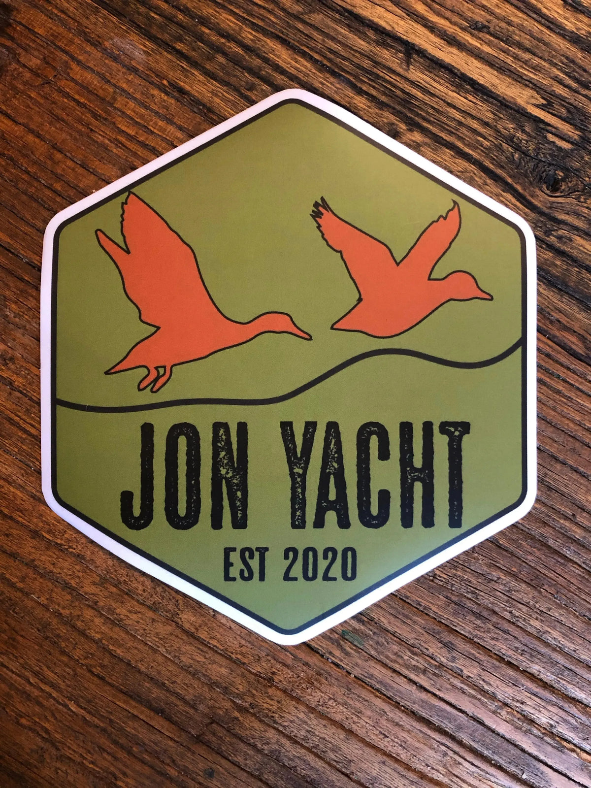 Hexagon sticker with two orange ducks flying over "JON YACHT EST 2020" text on an olive green background.