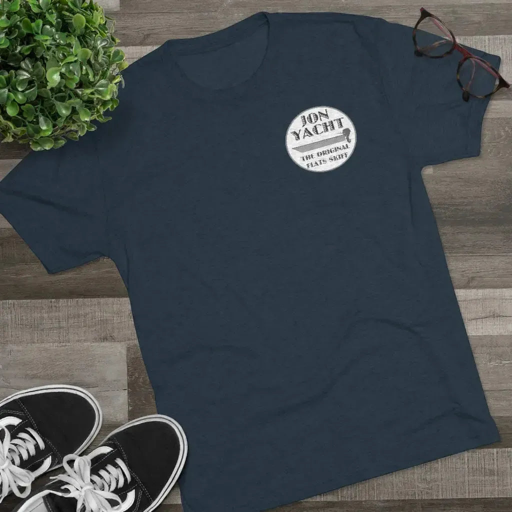 Navy blue "Jon Yacht The Original Flats Skiff" t-shirt with a white circular logo on a wooden surface.