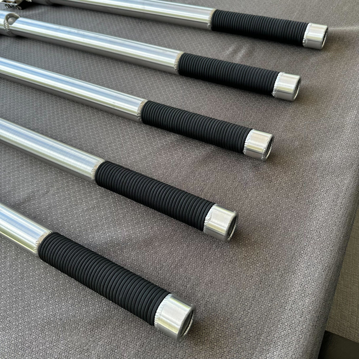 Five silver aluminum X-LONG tiller extension handles with black ribbed grips, shown on a gray fabric.