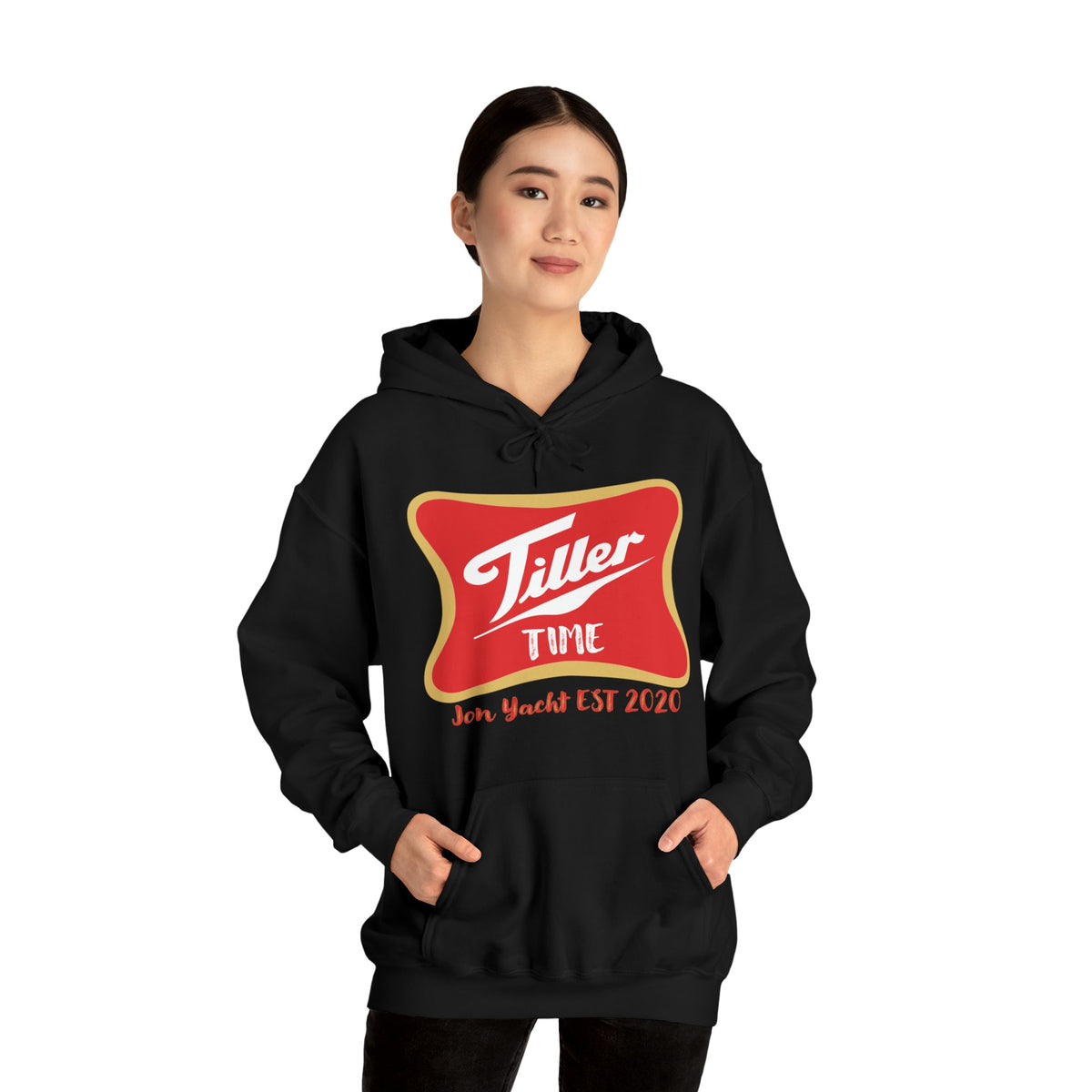 Woman wearing a black Tiller Time Hoodie with red and gold logo, hands in front kangaroo pocket.