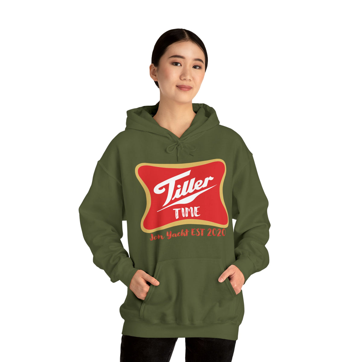 Woman wearing an olive green "Tiller Time" graphic hoodie with a red and gold emblem, hands in kangaroo pocket.