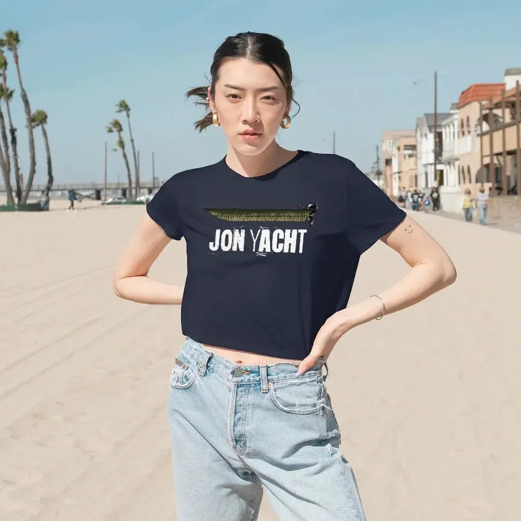 Woman in a navy flowy cropped tee with "JON YACHT" graphic, light wash jeans, on a sunny beach.