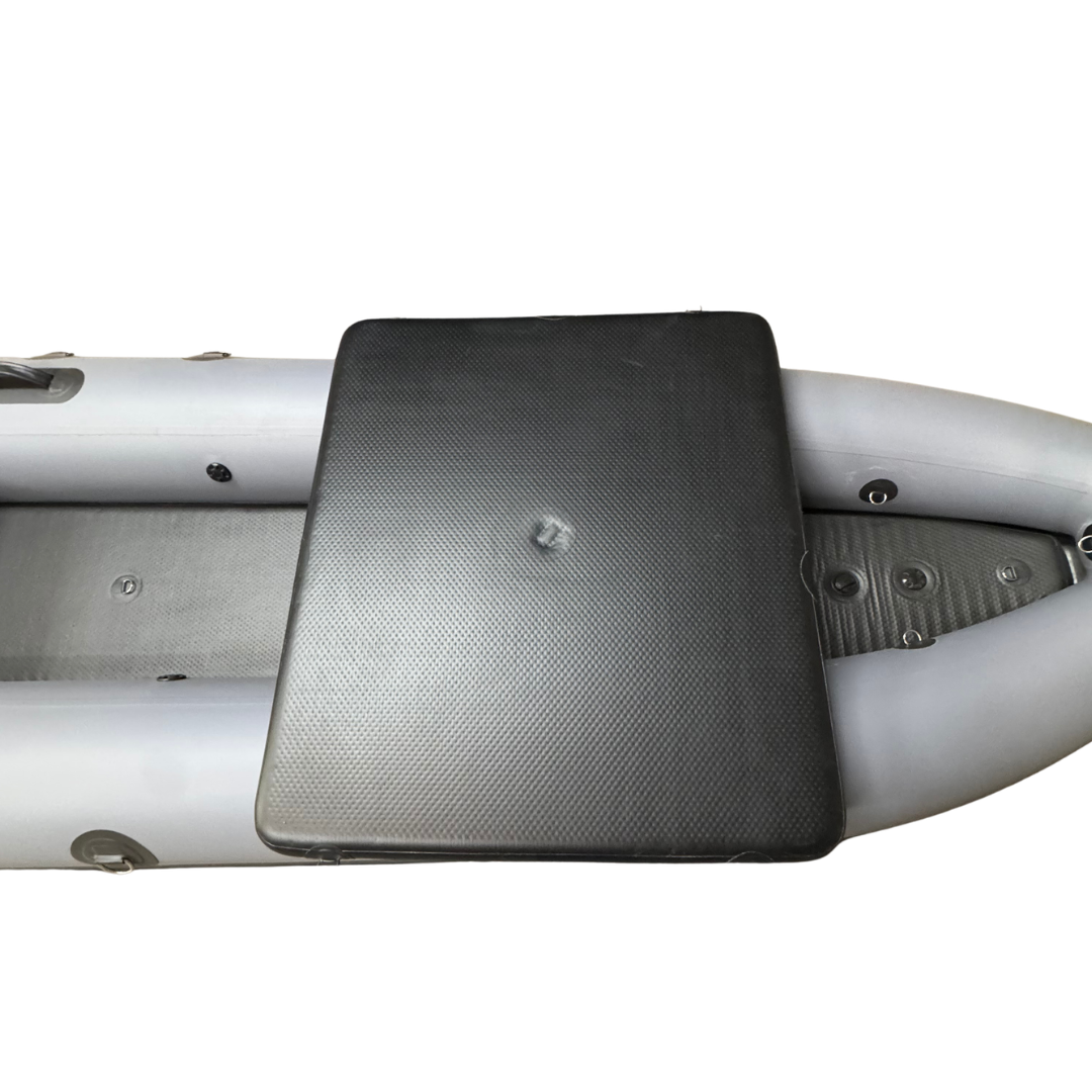 A black textured inflatable boat seat cushion placed on a light gray inflatable boat, isolated on a white background.