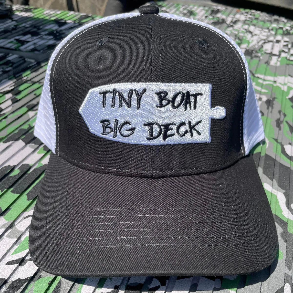 Black and white trucker hat with "Tiny Boat Big Deck" embroidered on a white patch.