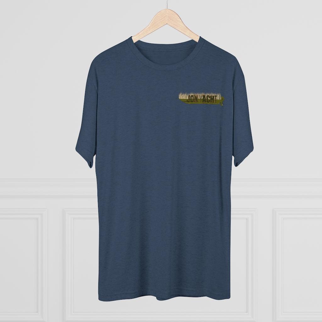 A navy blue short-sleeve t-shirt hanging on a light wood hanger against a white paneled wall. The shirt features a small graphic on the left chest with the text 'JON YACHT' in yellow on a camouflage background.