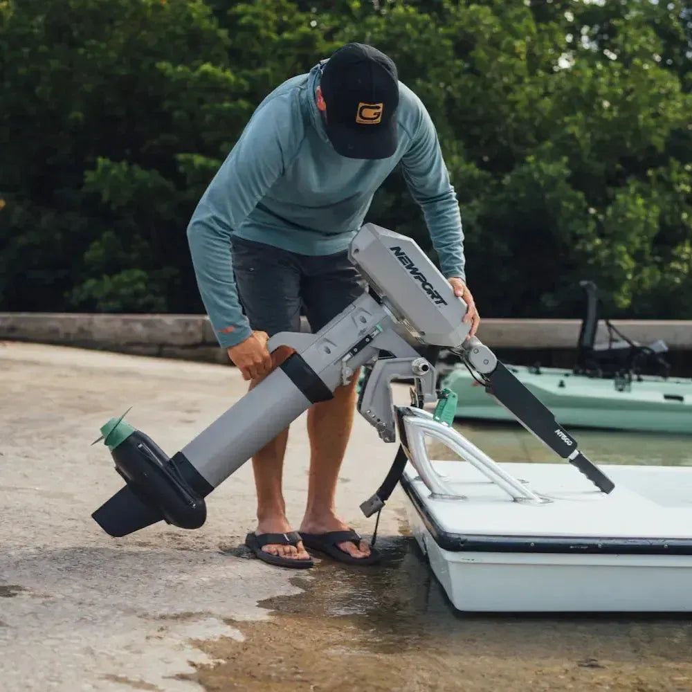 Man installing a gray Newport NT600 6hp electric outboard motor with a green propeller onto a small white boat.