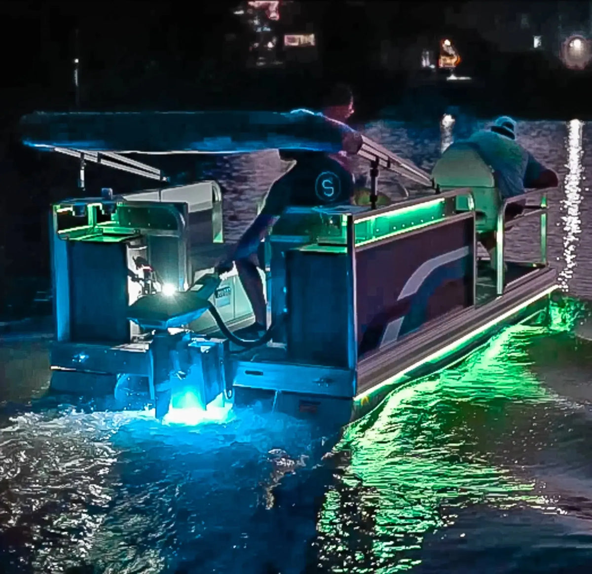 Pontoon boat at night with vibrant green and blue Plashlight RGBW flexible LED light strips illuminating the water.