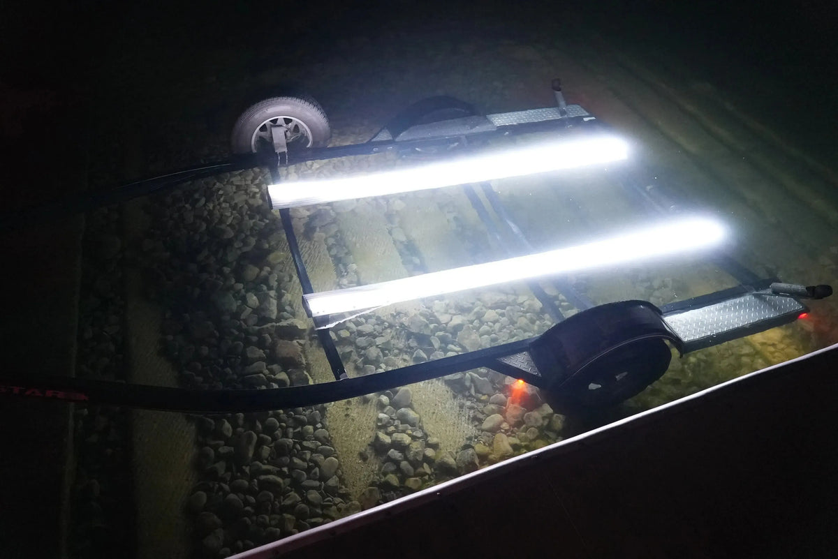 Two bright white Plashlight LED strips illuminate a boat trailer bunk board submerged in water.