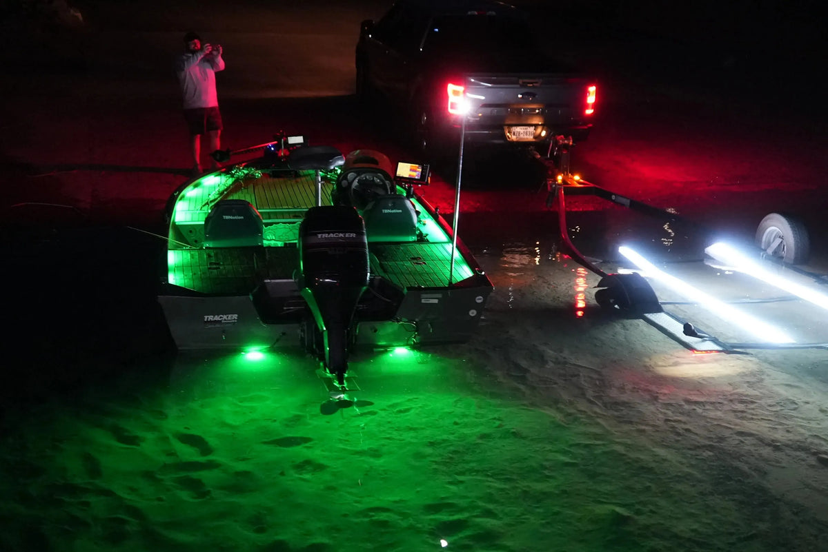Green LED light strips illuminate a boat and the water at night, with bright white lights on the trailer.