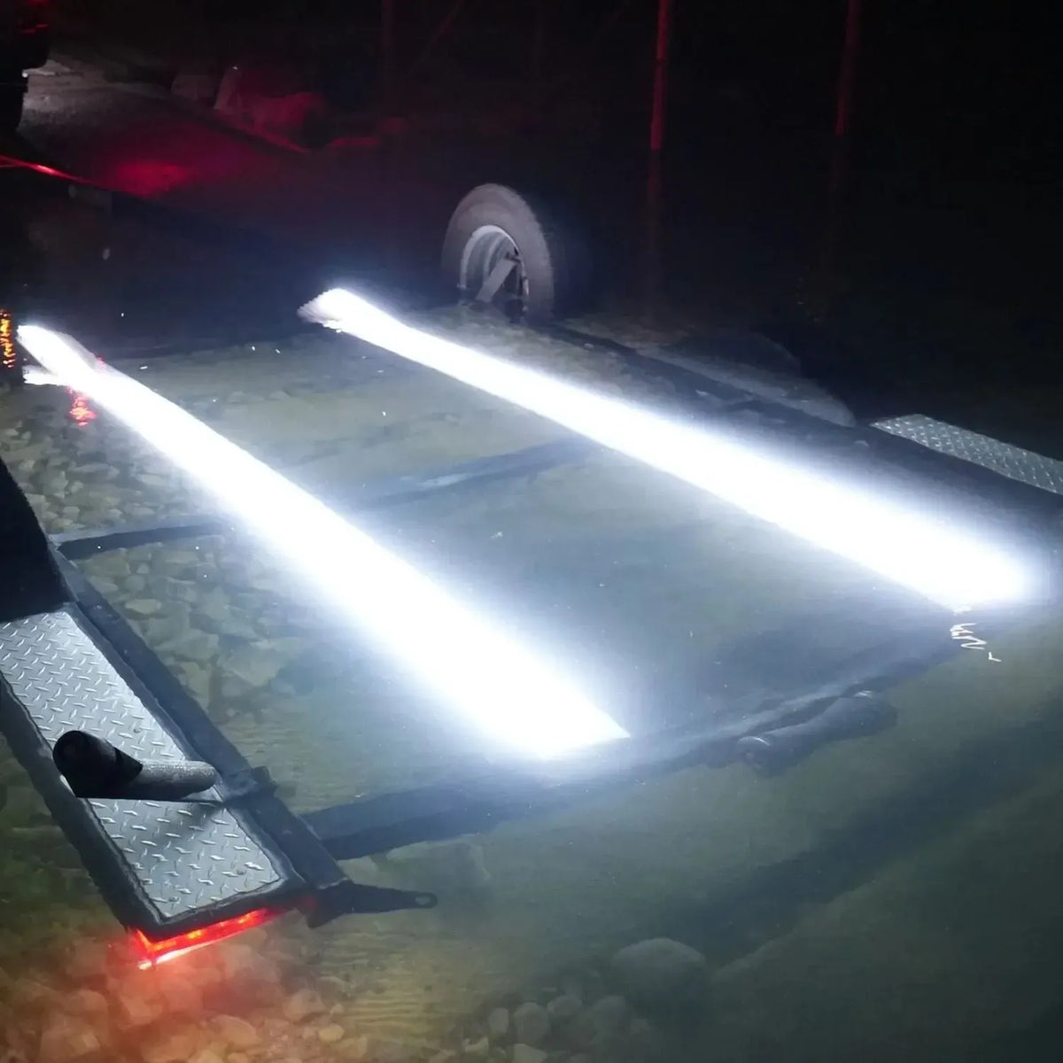 Two bright white Plashlight LED strips illuminating underwater bunk boards on a boat trailer at night.