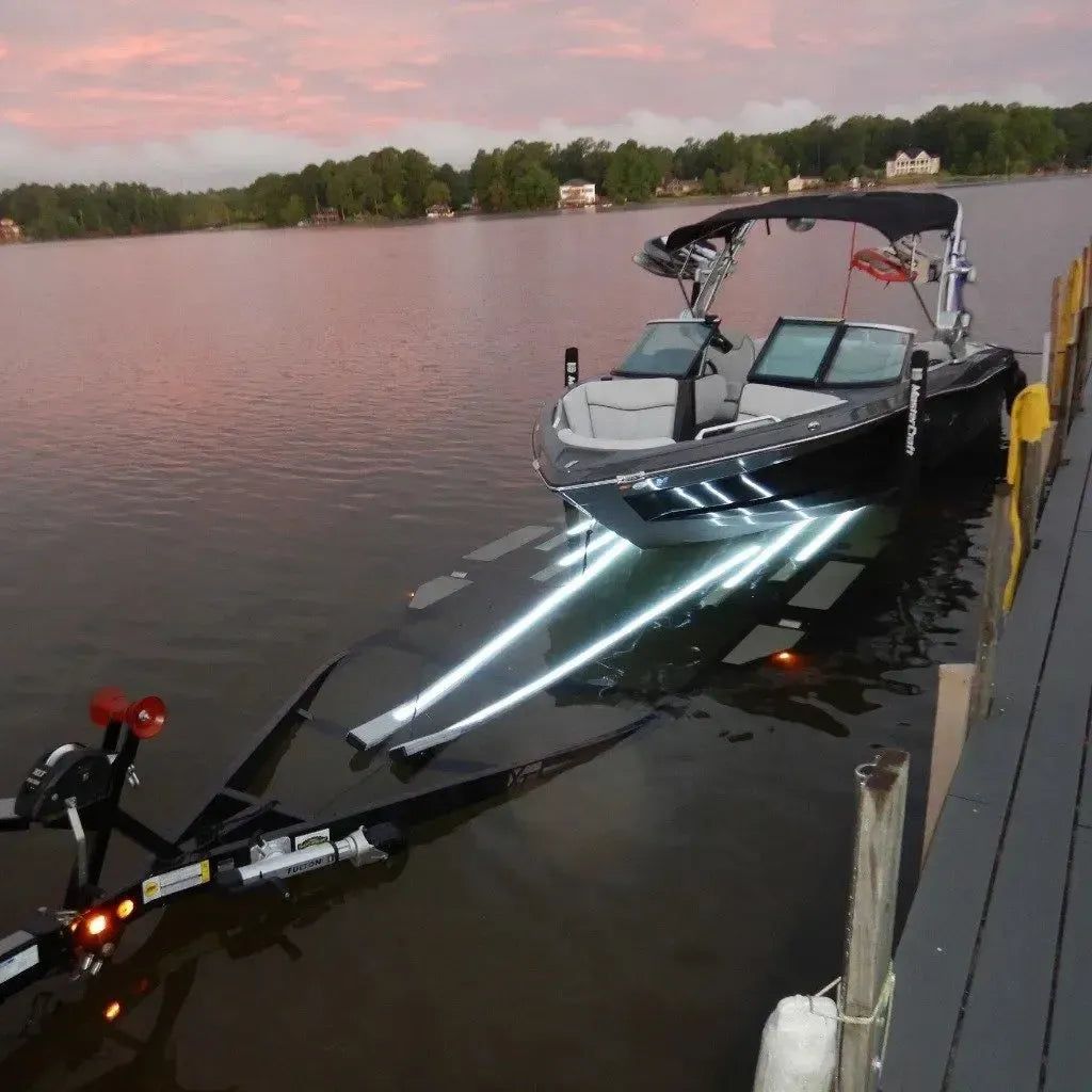 Black boat on a trailer with bright white LED light strips illuminating the water at dusk.