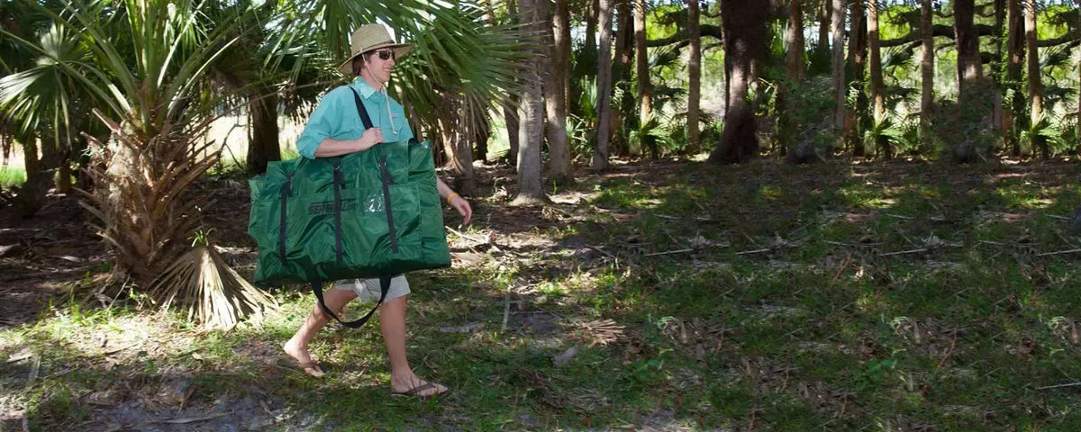 Man in a straw hat and green shirt carrying a packed Hunter Green Sea Eagle 285 frameless inflatable fishing boat.