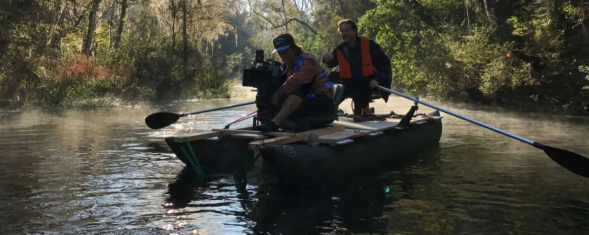 Two men in a dark hunter green Sea Eagle 375fc FoldCat inflatable pontoon fishing boat with oars on a misty river.