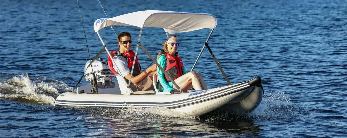 Two people in a white Sea Eagle 437ps PaddleSki inflatable catamaran with a canopy and motor on blue water.