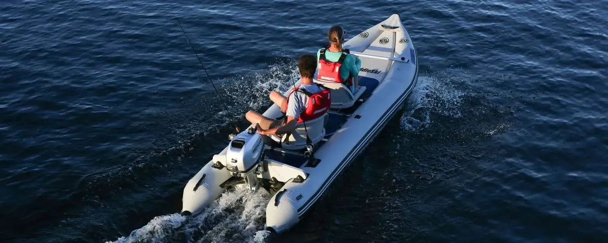 Two people in red life vests motor a white Sea Eagle 437ps PaddleSki inflatable catamaran on blue water.