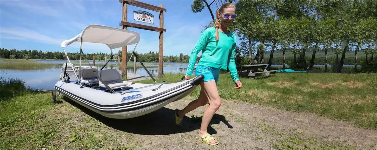 Woman carrying a white and gray Sea Eagle 437ps PaddleSki inflatable catamaran with a canopy.