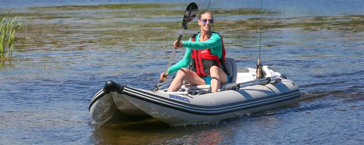 Woman paddling a gray Sea Eagle 437ps PaddleSki inflatable catamaran boat on calm water.