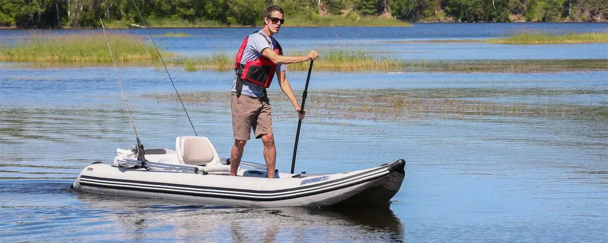 Man in red life vest paddling a gray Sea Eagle 437ps PaddleSki inflatable catamaran with fishing rods.