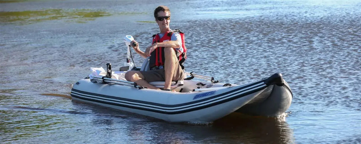 Man in red life vest operating a gray Sea Eagle 437ps PaddleSki inflatable catamaran with a trolling motor.