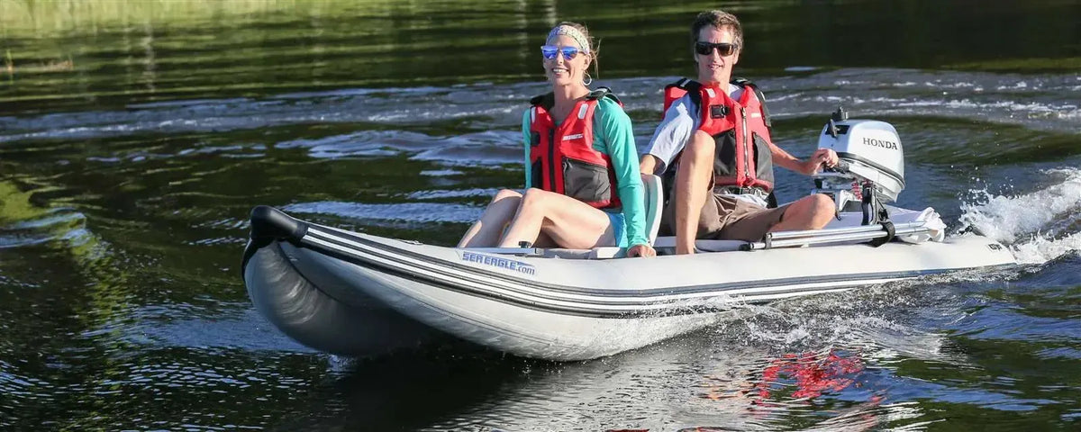 Two people in red life vests ride a gray Sea Eagle 437ps PaddleSki inflatable catamaran with a Honda motor.
