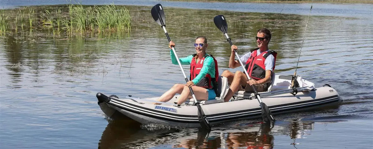 Two people paddling a gray Sea Eagle 437ps PaddleSki inflatable catamaran boat on a lake.