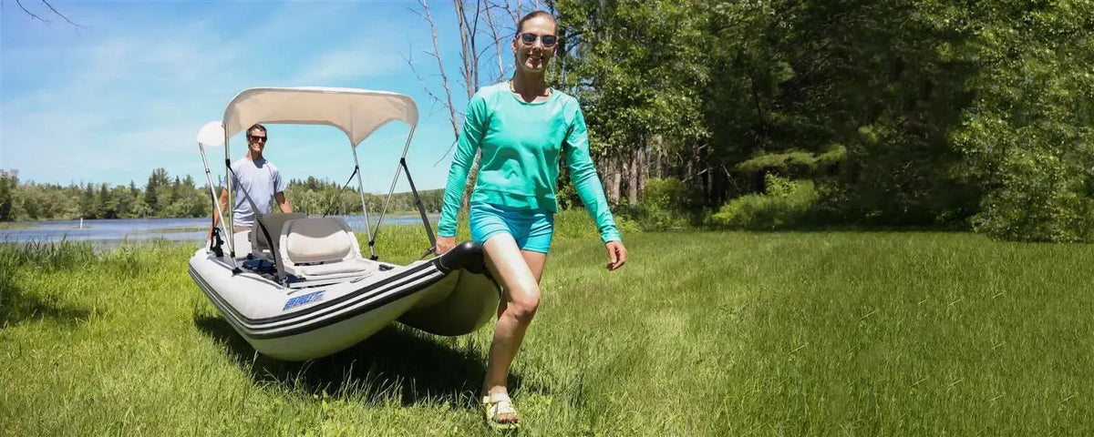 Two people carrying a tan and black Sea Eagle 437ps Paddleski inflatable boat with a white canopy across green grass.