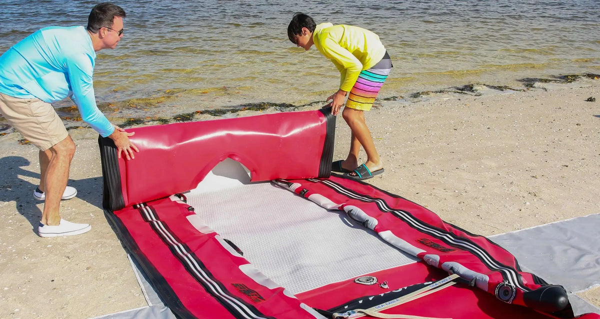 Man and boy assembling a red Sea Eagle FastCat14 inflatable catamaran on a sandy beach.