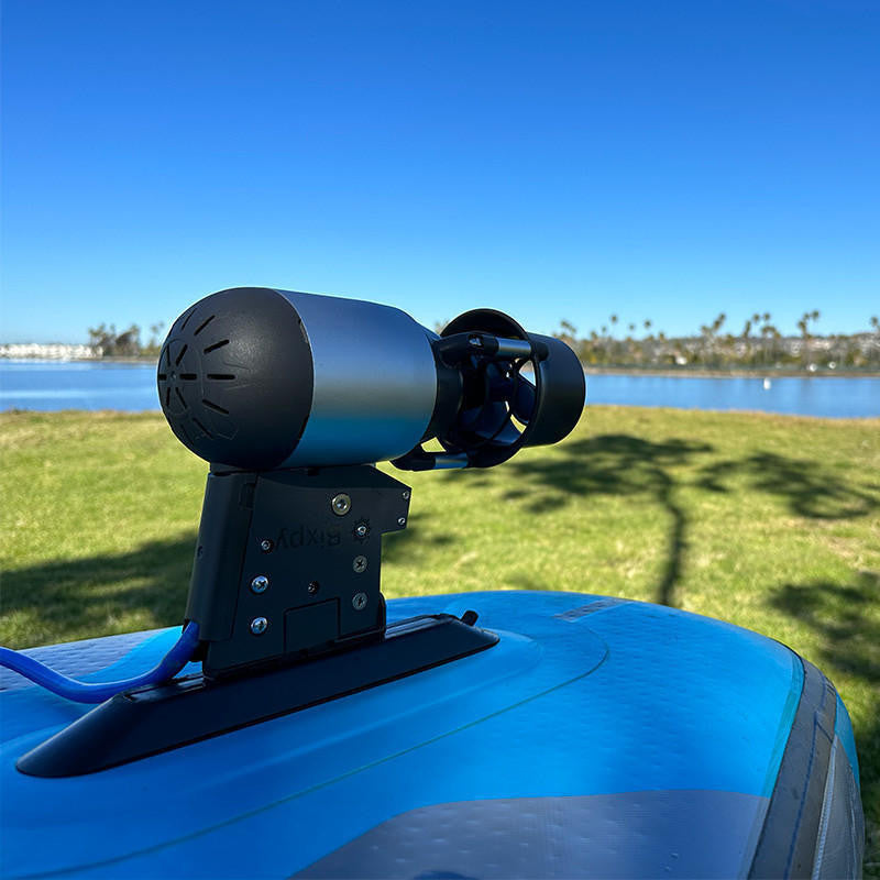 Blue vehicle with a mounted device against a clear blue sky and grassy area.