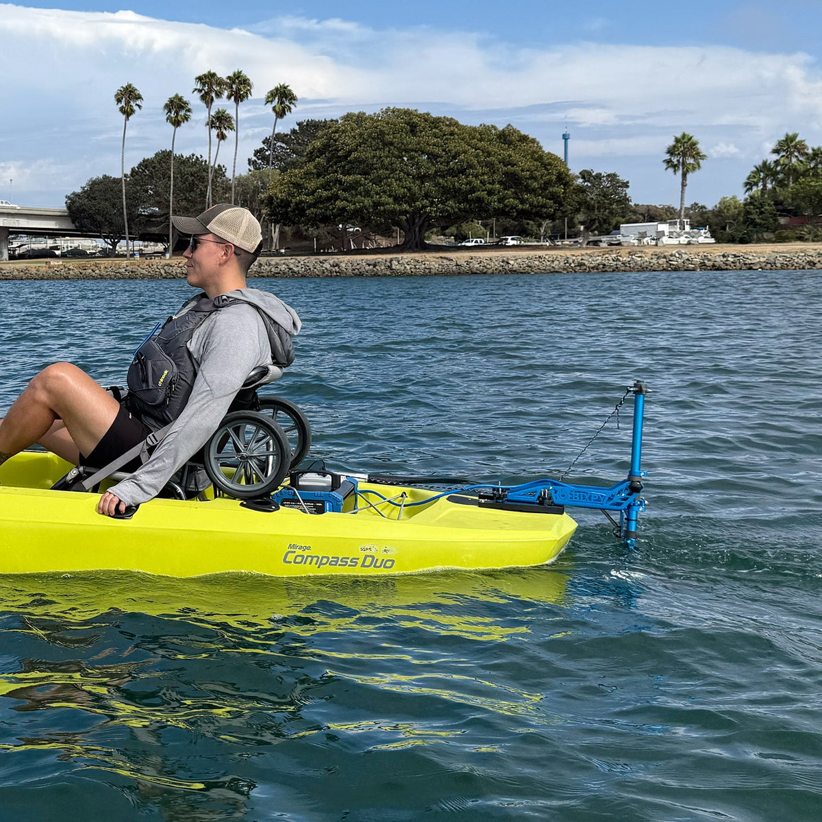 Person in a wheelchair using a yellow kayak with an attached motor on a body of water.