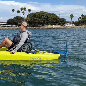 Person in a wheelchair using a yellow kayak with an attached motor on a body of water.