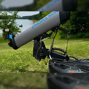 A large ePropulsion kLite 7500 outboard motor mounted on a black tracking mount and motorized base, photographed outdoors on grass near a lake with trees in the background.