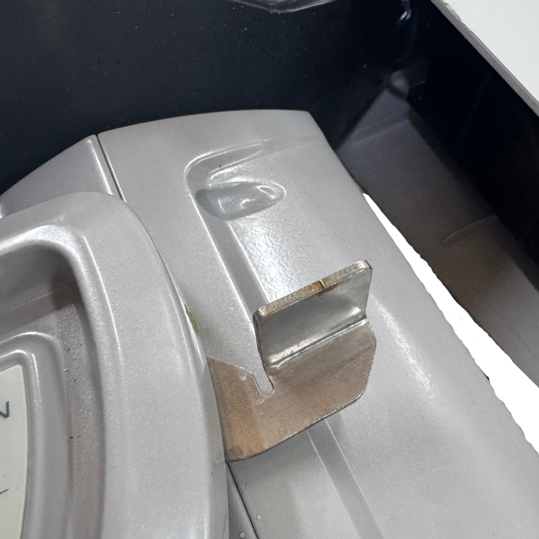 A close-up shot of a epropulsion silver appliance component, likely a dryer or washing machine door panel, featuring a metal latch and a small piece of brown tape applied to a seam.