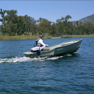 Person driving a small Bixpy boat on a lake with trees and mountains in the background