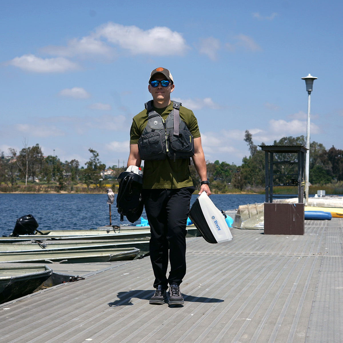 Person walking on a dock with fishing gear, wearing a green shirt and black pants.
