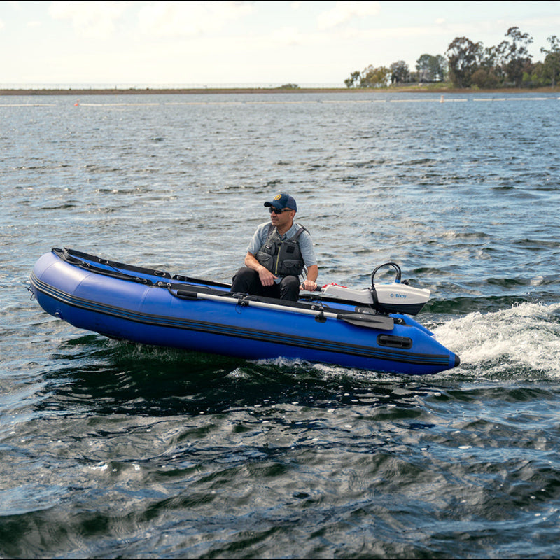 Person in a blue inflatable boat on a body of water with trees in the background