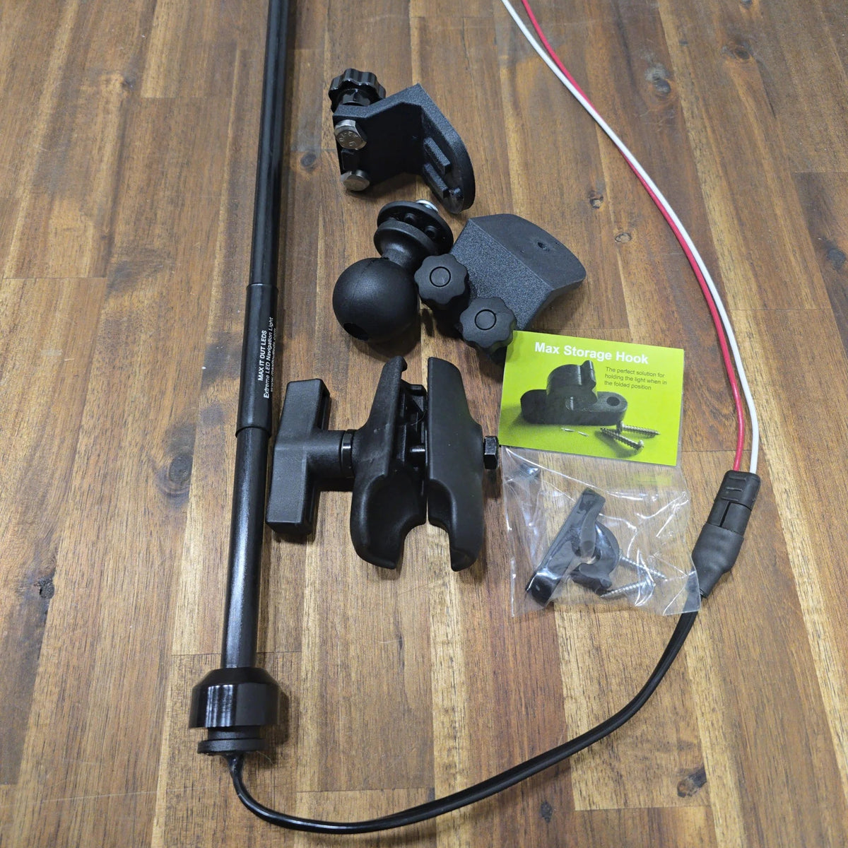 Disassembled 45° T-Bolt Mount Package components laid out on a wooden surface, featuring the LED navigation light pole, wiring harness, ball mount, double-socket clamp arm, angled track brackets, and packaged Max Storage Hook kit.