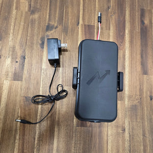 Max It Out LEDs Max Kayak Power System closed battery case with side latch clips and power cable, shown next to an AC wall charger on a wooden table.
