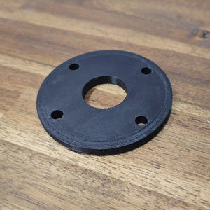 Black circular mounting base plate spacer with four screw holes and a center pass-through hole for the Max It Out LEDs Premier Universal LED Stern Light Kit, resting on a wooden surface.
