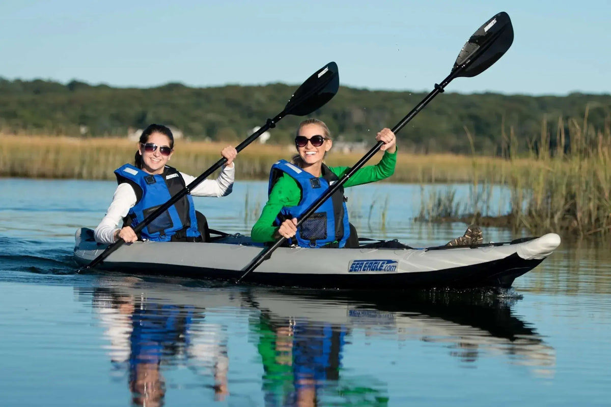 Two women paddling a gray and white Sea Eagle FastTrack inflatable kayak with black paddles.