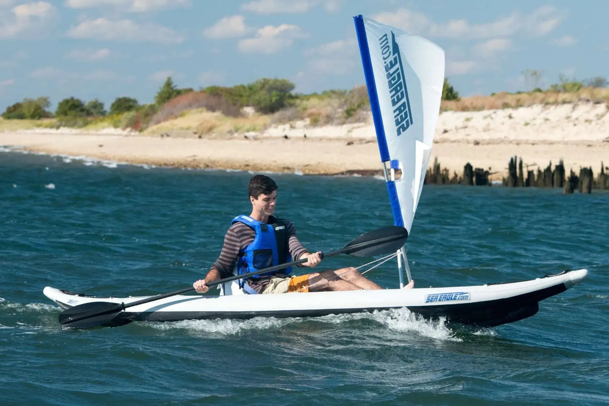 Man in a blue life vest paddling a white and black Sea Eagle FastTrack inflatable kayak with a sail.