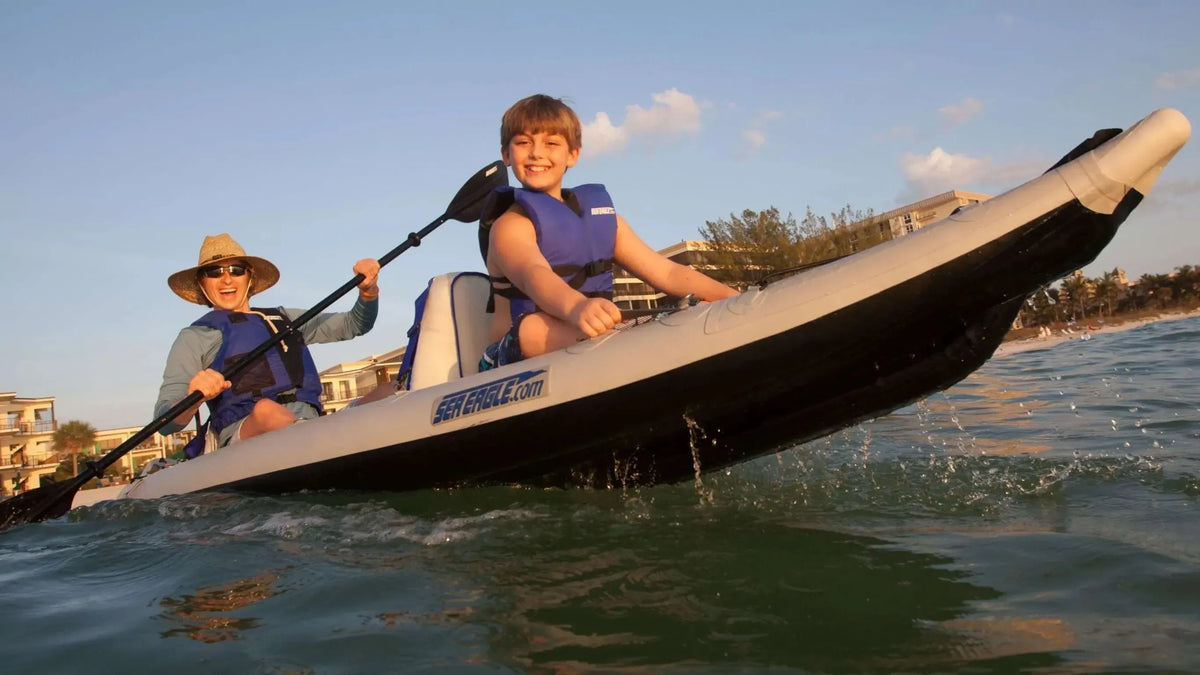 Two people in a gray and black Sea Eagle 385ft FastTrack inflatable kayak on the water, paddling.