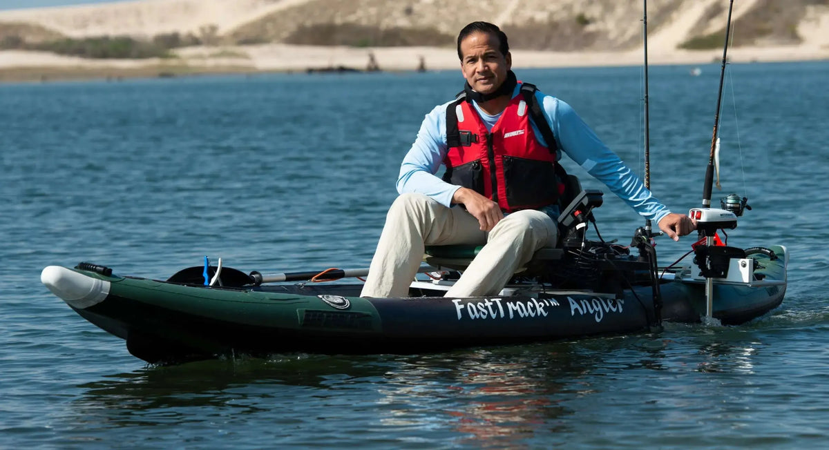 Man in a red life vest paddling a dark green Sea Eagle FastTrack Angler inflatable kayak with fishing rods.