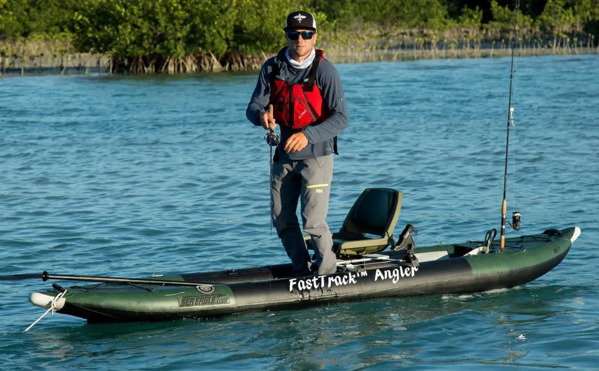 Man stands on a green and black Sea Eagle FastTrack Angler inflatable kayak with fishing rods.