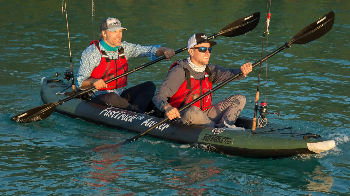 Two men paddle a green Sea Eagle 385fta FastTrack Angler inflatable kayak with fishing rods on calm water.