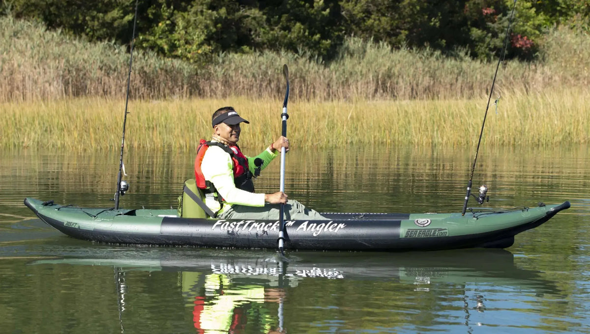 Green Sea Eagle 385fta FastTrack Angler inflatable kayak with a paddler and fishing rods on calm water.