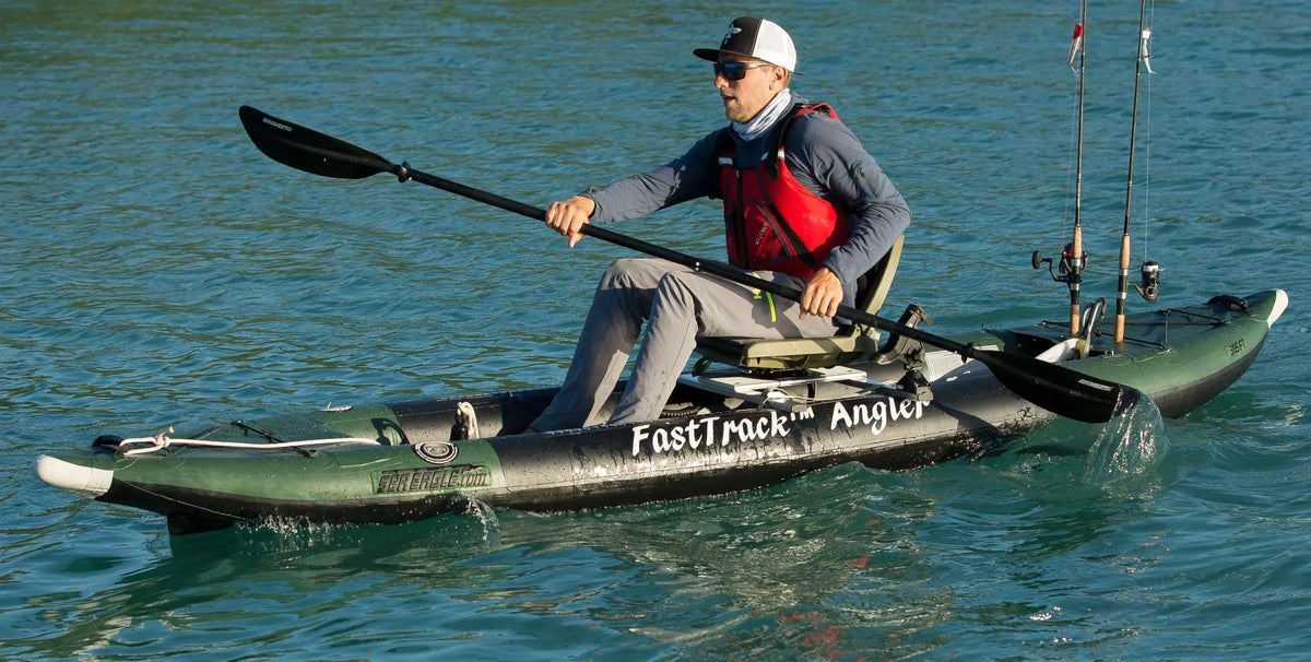 Man paddling a green and black Sea Eagle 385fta FastTrack Angler inflatable kayak with fishing rods.