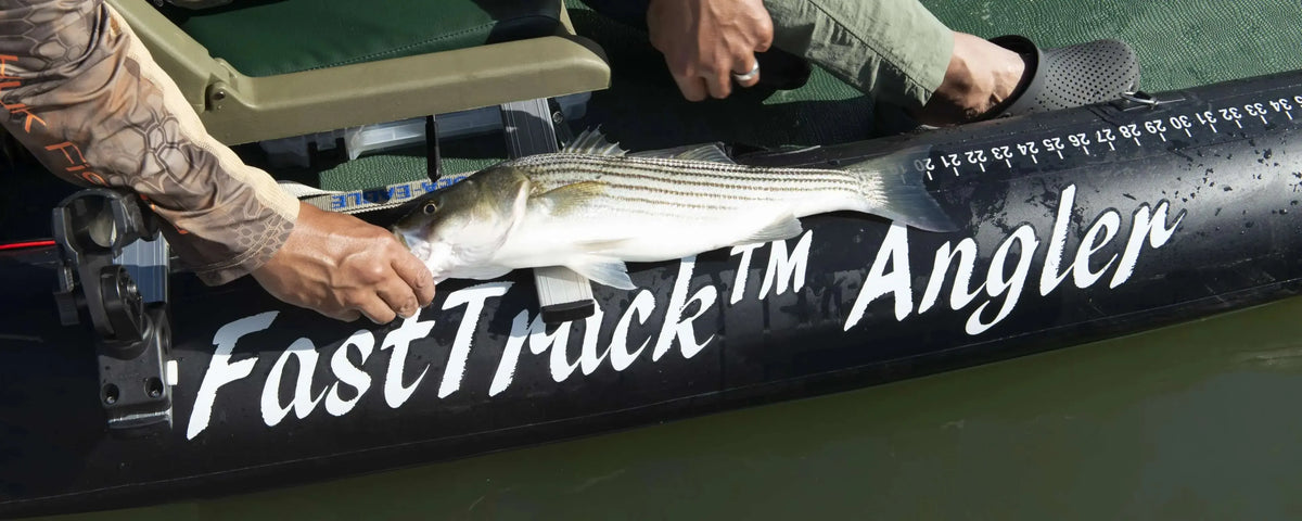 Angler holding a striped bass on a black Sea Eagle FastTrack™ inflatable kayak with a measuring ruler.