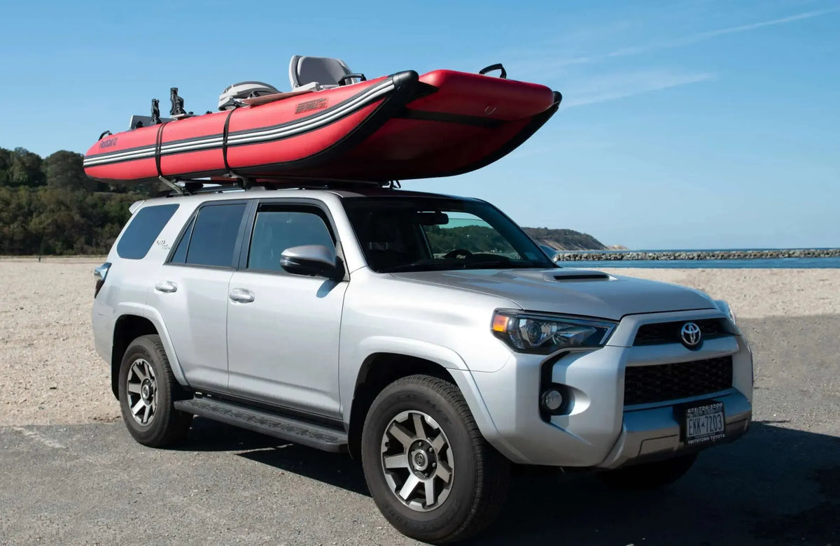 Red Sea Eagle FastCat12 inflatable catamaran boat on a silver SUV roof rack at the beach.