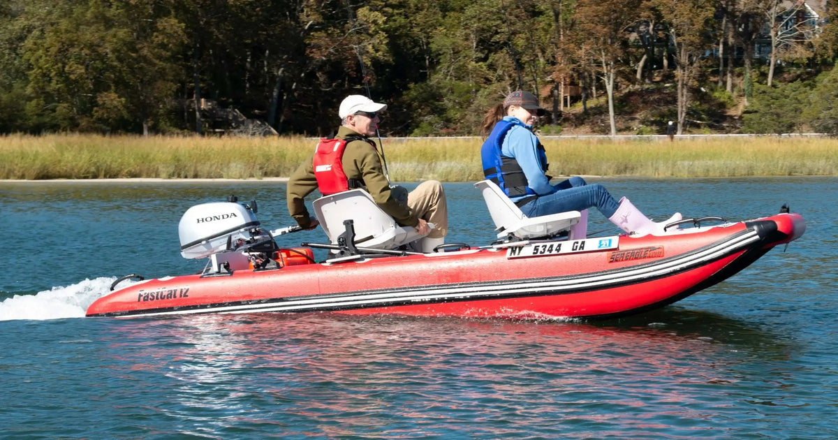 Two people on a red Sea Eagle FastCat12 inflatable catamaran with a Honda outboard motor on the water.